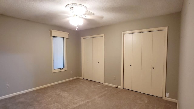 unfurnished bedroom with carpet, a textured ceiling, baseboards, and two closets