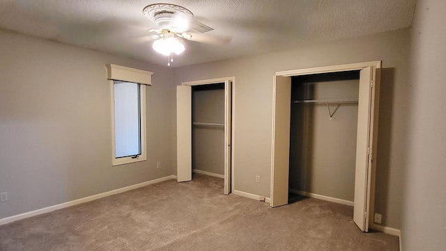 unfurnished bedroom with baseboards, ceiling fan, a textured ceiling, carpet flooring, and multiple closets