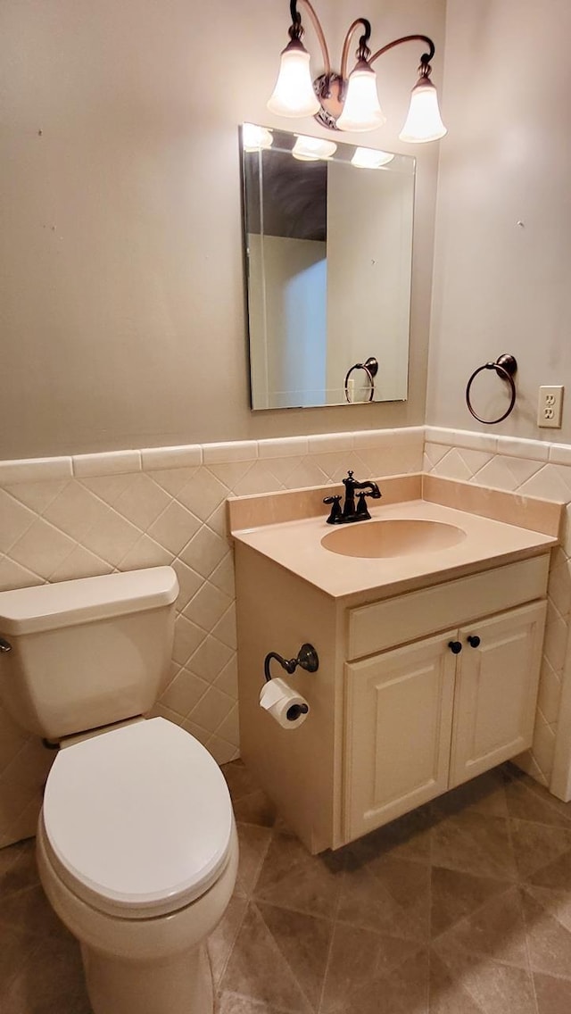 half bath featuring wainscoting, toilet, tile patterned floors, vanity, and tile walls