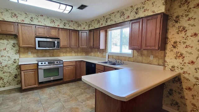 kitchen featuring stainless steel appliances, light countertops, visible vents, a sink, and wallpapered walls