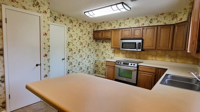 kitchen featuring wallpapered walls, appliances with stainless steel finishes, light countertops, a textured ceiling, and a sink