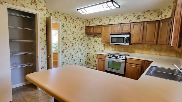 kitchen featuring wallpapered walls, a peninsula, stainless steel appliances, light countertops, and a sink