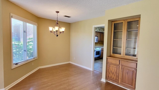 unfurnished dining area with a textured ceiling, a notable chandelier, visible vents, baseboards, and dark wood finished floors