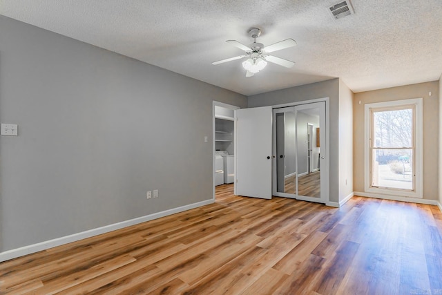 unfurnished bedroom featuring a textured ceiling, wood finished floors, visible vents, baseboards, and washer and dryer