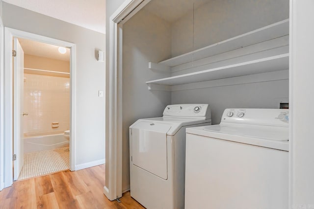 clothes washing area featuring baseboards, washing machine and dryer, and light wood-style floors