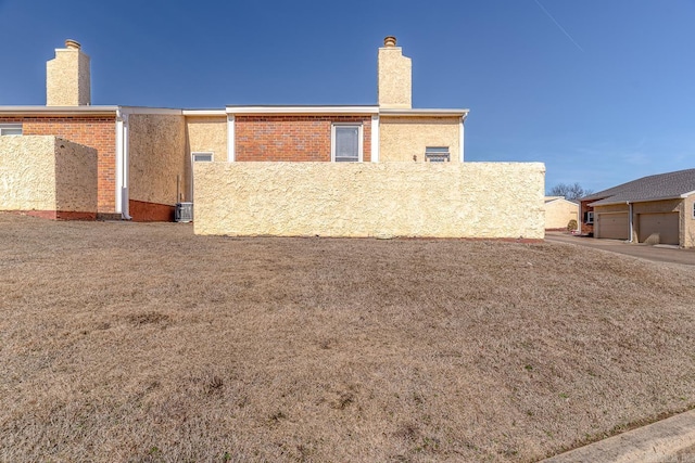 back of house with brick siding, a chimney, and stucco siding