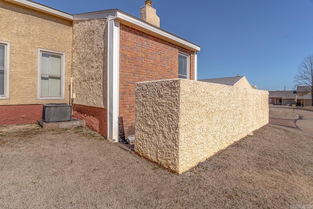 view of side of property with stucco siding, a chimney, and brick siding