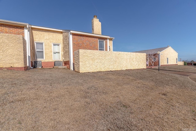 rear view of property featuring brick siding, a chimney, central AC unit, and stucco siding