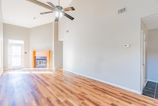 unfurnished living room with light wood-type flooring, high vaulted ceiling, visible vents, and a tile fireplace