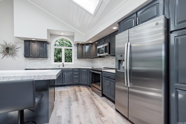 kitchen featuring crown molding, backsplash, appliances with stainless steel finishes, light wood-type flooring, and vaulted ceiling with skylight