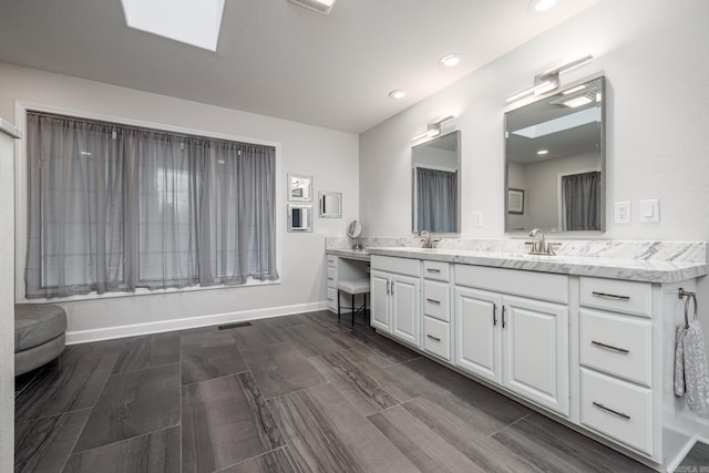 bathroom featuring a skylight, double vanity, visible vents, a sink, and baseboards
