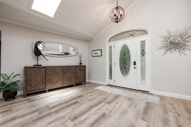 foyer with light wood-style flooring, a notable chandelier, baseboards, vaulted ceiling, and crown molding