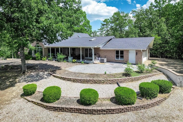 rear view of property featuring driveway, central AC unit, a sunroom, roof with shingles, and brick siding