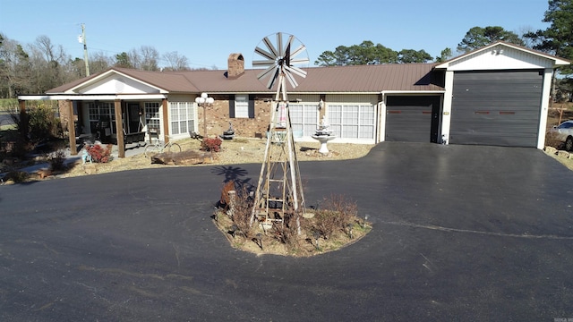 ranch-style home featuring metal roof, driveway, a chimney, and an attached garage