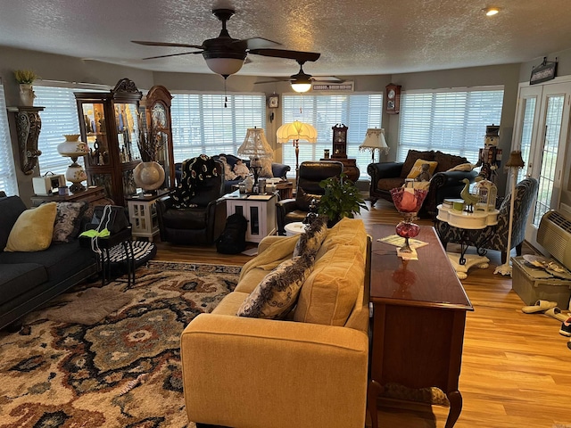 living room with a textured ceiling, light wood-type flooring, a wealth of natural light, and a ceiling fan