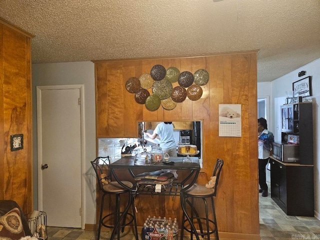 kitchen with a textured ceiling, brown cabinetry, and wooden walls