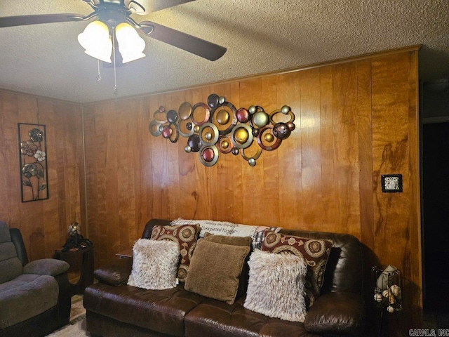 living room featuring wooden walls, ceiling fan, and a textured ceiling