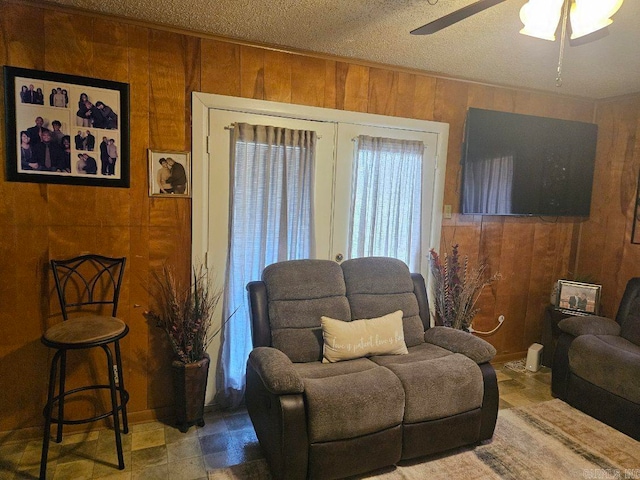 sitting room with wooden walls, a ceiling fan, and a textured ceiling