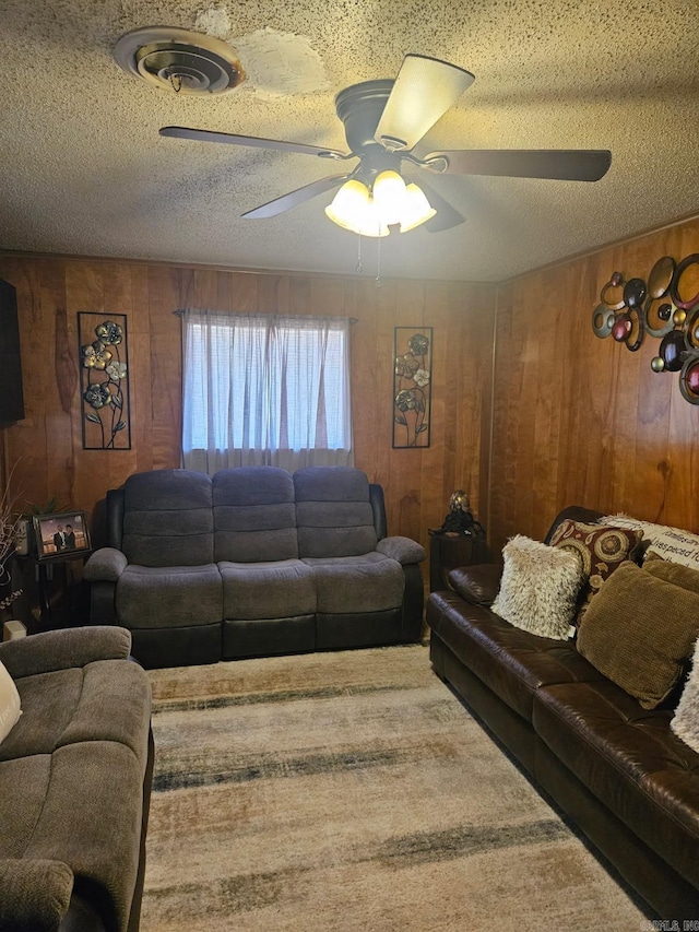 living area with ceiling fan, wood walls, and a textured ceiling