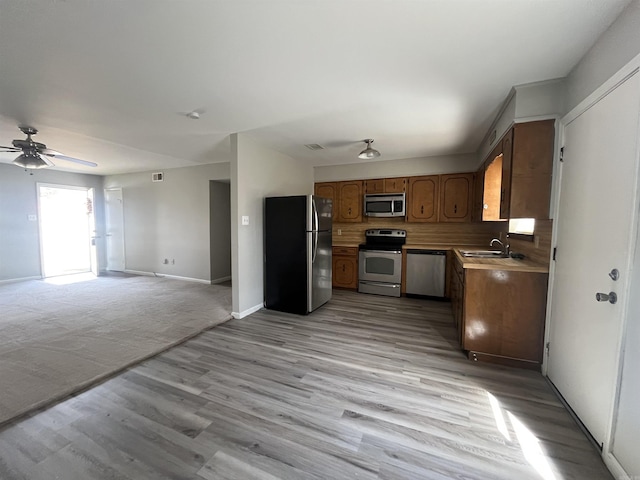 kitchen with light wood finished floors, tasteful backsplash, appliances with stainless steel finishes, open floor plan, and a sink