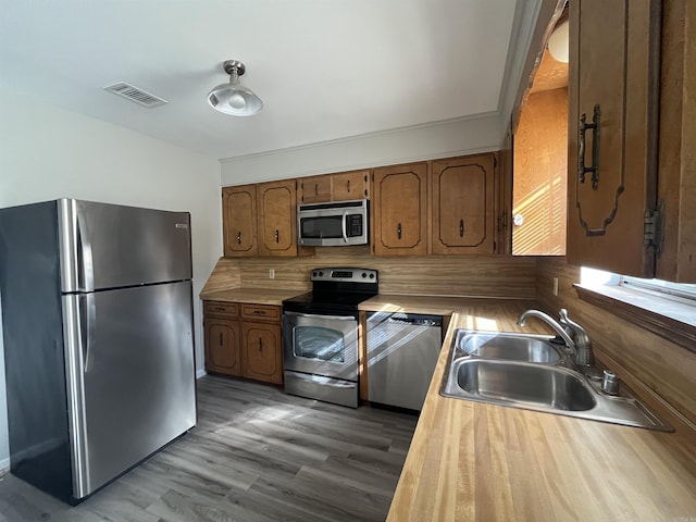 kitchen featuring wood finished floors, a sink, visible vents, appliances with stainless steel finishes, and brown cabinetry