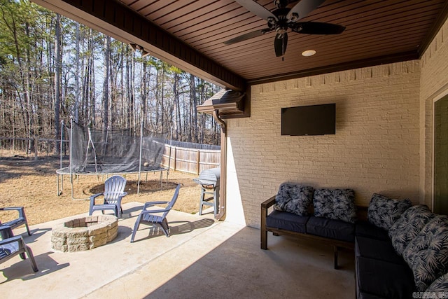 view of patio / terrace with an outdoor fire pit, a trampoline, fence, and ceiling fan