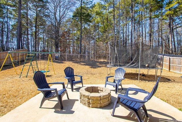 view of patio featuring a trampoline, a fire pit, a playground, and a fenced backyard