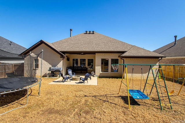 back of house with a fire pit, a trampoline, fence, a patio area, and brick siding