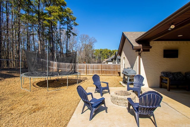 exterior space with an outdoor fire pit, a trampoline, fence, and a grill