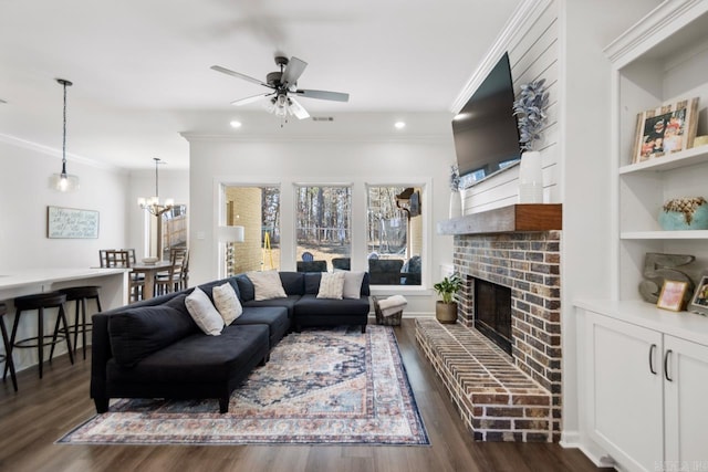 living area with a fireplace, crown molding, visible vents, dark wood-type flooring, and ceiling fan with notable chandelier