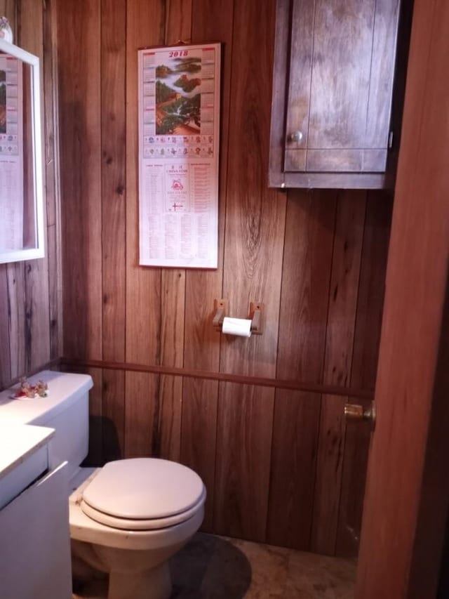 half bathroom featuring wood walls, vanity, and toilet