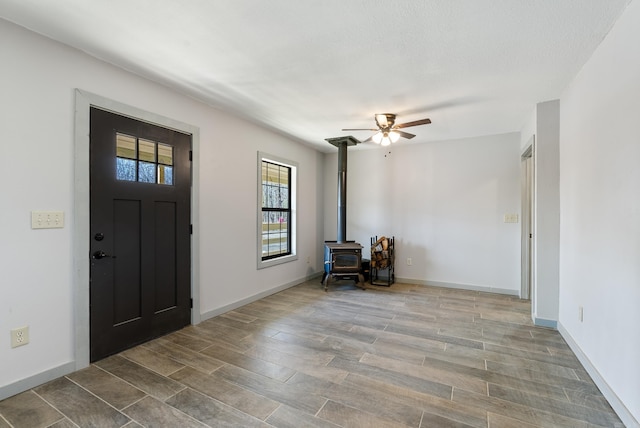 foyer entrance featuring a wood stove, baseboards, and wood finished floors