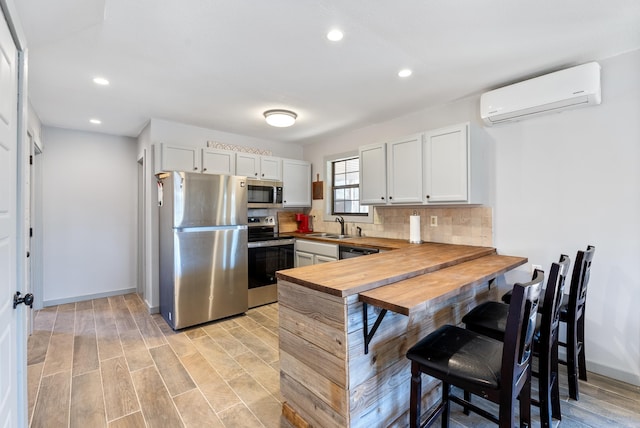 kitchen with a wall unit AC, butcher block countertops, a sink, appliances with stainless steel finishes, and tasteful backsplash