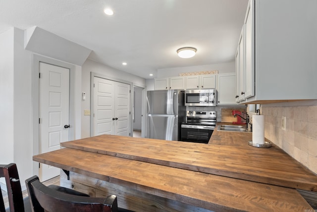 kitchen featuring stainless steel appliances, tasteful backsplash, a sink, butcher block countertops, and a peninsula