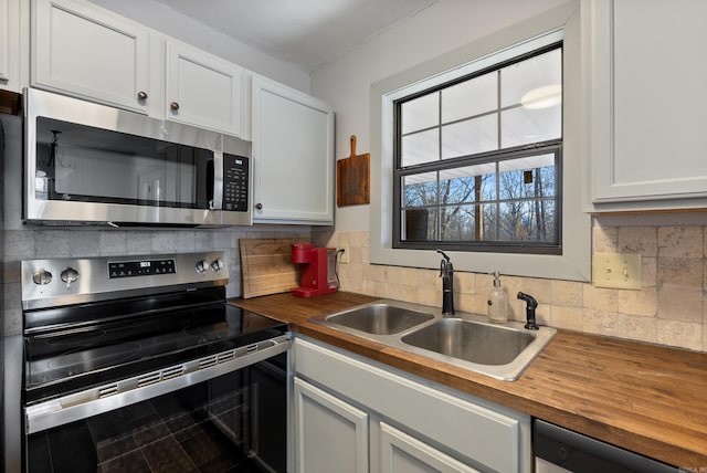 kitchen featuring backsplash, appliances with stainless steel finishes, white cabinets, a sink, and wood counters