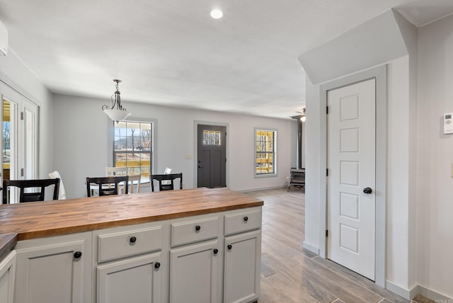 kitchen with decorative light fixtures, light wood finished floors, wooden counters, a wood stove, and white cabinetry