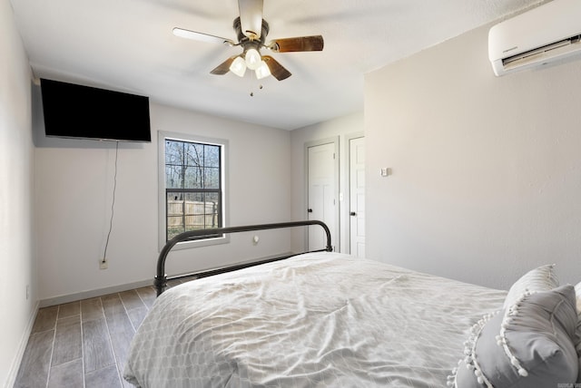 bedroom with ceiling fan, baseboards, wood finished floors, and a wall mounted AC