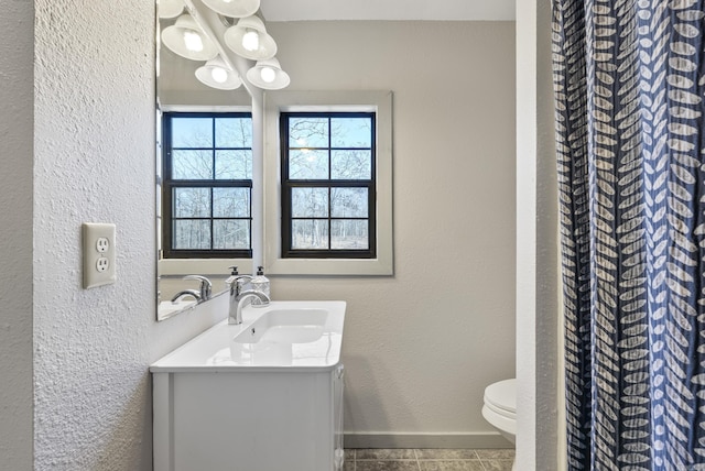 bathroom featuring a textured wall, vanity, toilet, and baseboards