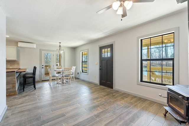 foyer featuring a wall unit AC, a ceiling fan, baseboards, light wood finished floors, and a wood stove