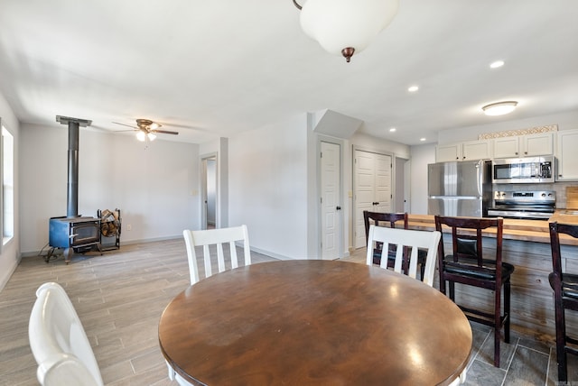 dining area featuring light wood finished floors, baseboards, ceiling fan, a wood stove, and recessed lighting