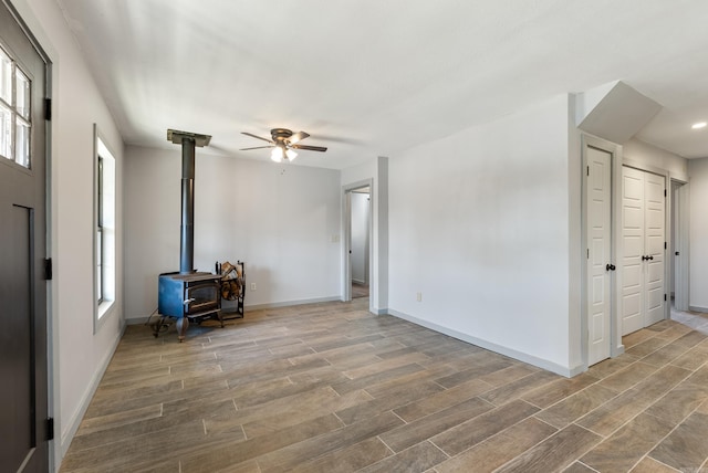 unfurnished living room featuring a healthy amount of sunlight, a wood stove, baseboards, and wood finished floors