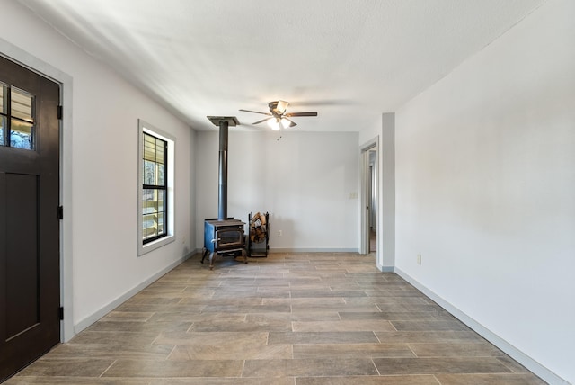 interior space featuring a wood stove, ceiling fan, baseboards, and wood finished floors