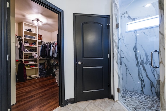 full bath with a walk in closet, a marble finish shower, and wood finished floors