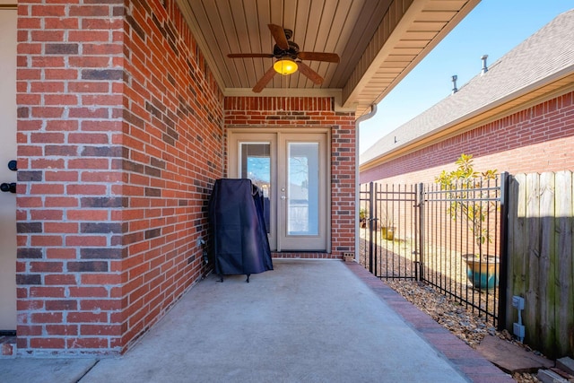 view of exterior entry featuring a ceiling fan, brick siding, and fence