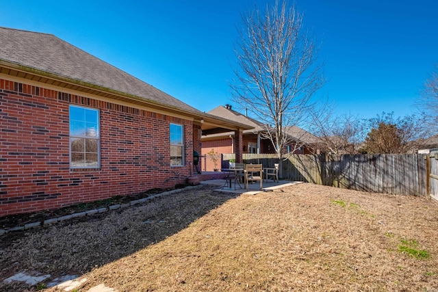 exterior space with fence private yard, brick siding, a patio, and roof with shingles