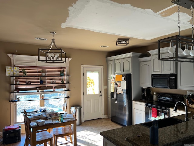 kitchen with dark stone countertops, hanging light fixtures, a notable chandelier, black appliances, and a sink