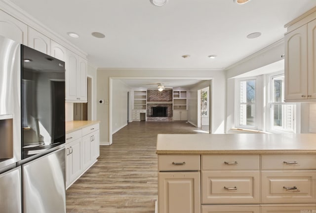 kitchen featuring a large fireplace, light countertops, stainless steel refrigerator with ice dispenser, and crown molding