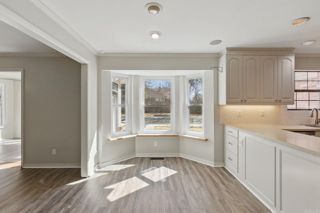 unfurnished dining area with light wood-style floors, baseboards, ornamental molding, and a sink