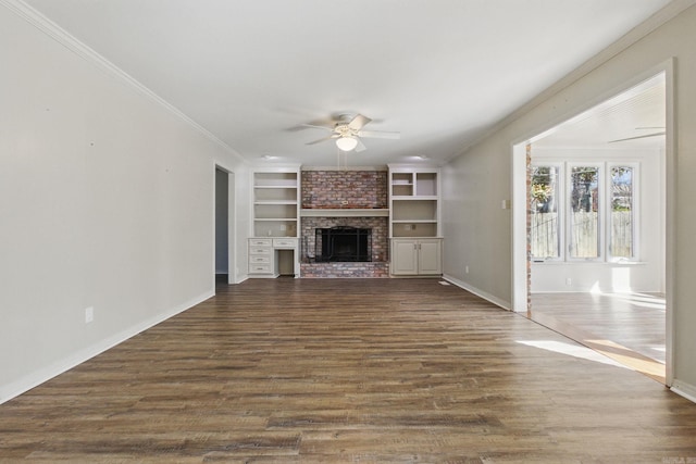 unfurnished living room with a ceiling fan, dark wood-type flooring, crown molding, built in shelves, and a fireplace