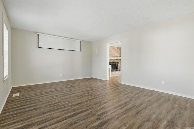 empty room featuring dark wood-type flooring, a brick fireplace, visible vents, and baseboards